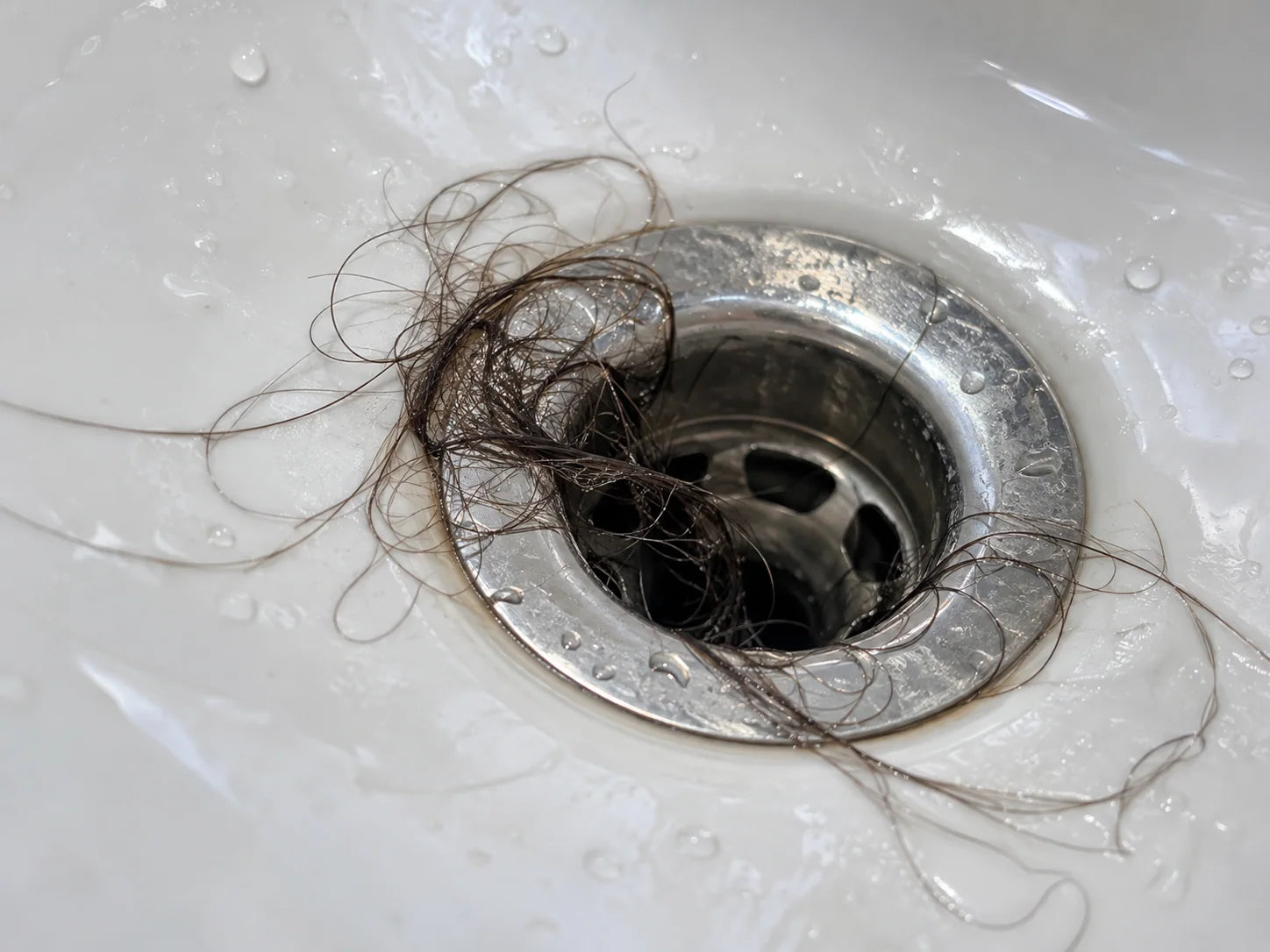 Illustrative strands of hair collecting around an open bathroom basin drain