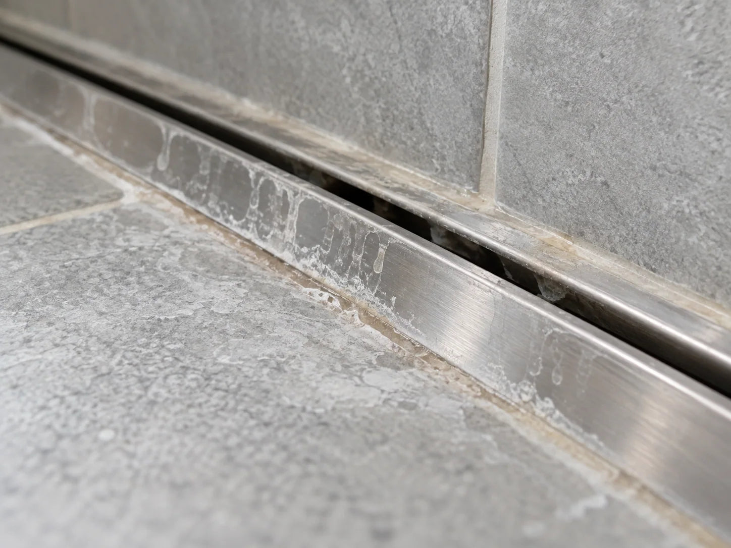 Illustrative chalky soap residue along a shower floor drain